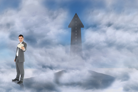 Businessman presenting banknotes against road turning into arrowの写真素材