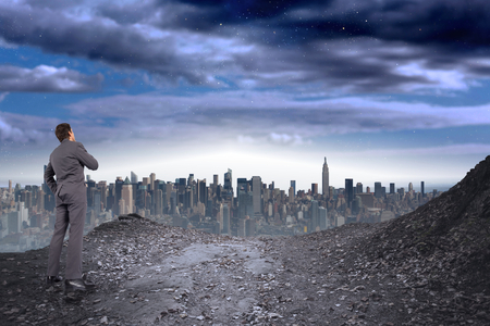 Thinking businessman with hand on chin against large city on the horizonの写真素材