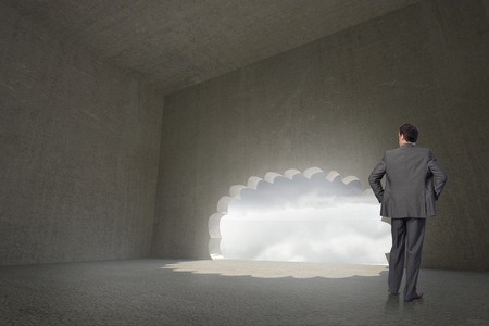 Businessman with hands on hips against cloud door in dark roomの写真素材