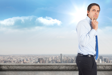 Thinking businessman touching his chin against balcony overlooking cityの写真素材