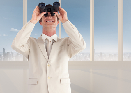 Confident businessman with binoculars against bright white room with windowsの写真素材