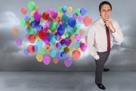 Thinking businessman touching his chin against many colourful balloons in cloudy roomの写真素材