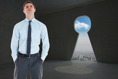 Serious businessman standing with hands in pockets against keyhole door in dark roomの写真素材