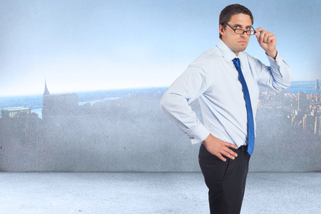 Thinking businessman tilting glasses against city scene in a roomの写真素材