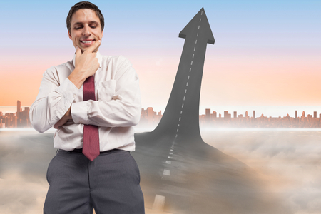 Thoughtful businessman with hand on chin against road turning into arrowの写真素材