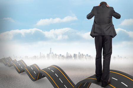 Stressed businessman with hands on head against bumpy road backdropの写真素材
