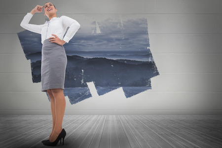 Smiling thoughtful businesswoman against display on wall showing mountain landscapeの写真素材