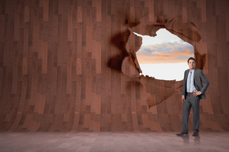 Smiling businessman with hand on hip against rip on wall showing bright skyの写真素材