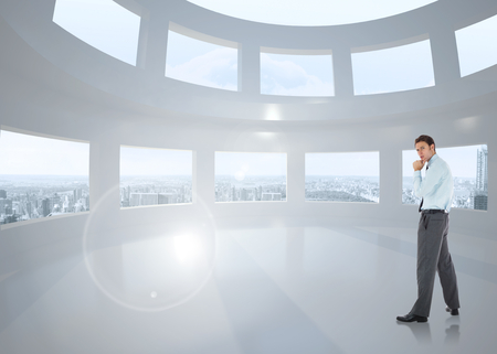 Thoughtful businessman with hand on chin against bright white room with windowsの写真素材