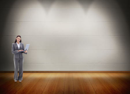 Businesswoman smiling with a laptop against room with wooden floorの写真素材
