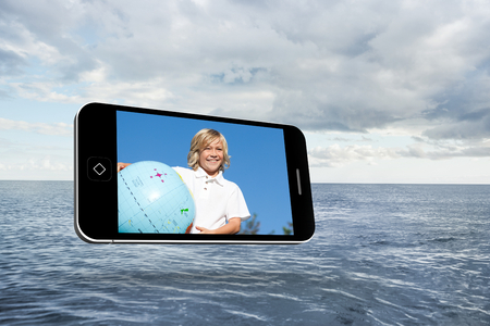 Blonde happy boy on smartphone screen against cloudy sky and oceanの写真素材