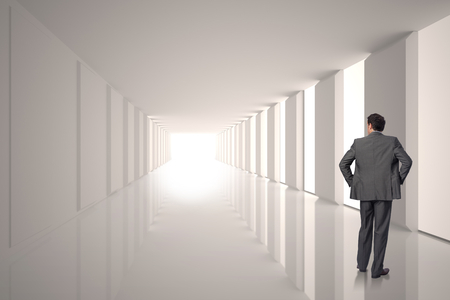 Businessman with hands on hips against lit up white modern hallwayの写真素材