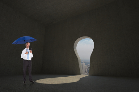 Happy businessman holding umbrella against keyhole door in dark roomの写真素材