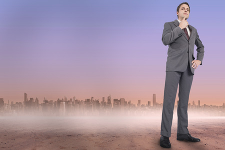 Thinking businessman with hand on chin against cityscape on the horizonの写真素材