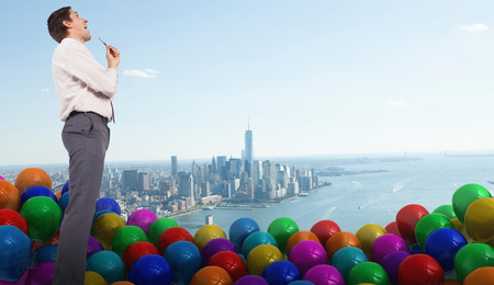 Thinking businessman holding pen against many colourful balloons against coast
