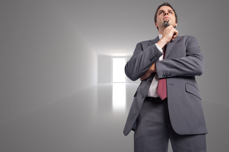 Thinking businessman holding his glasses against bright hallの写真素材