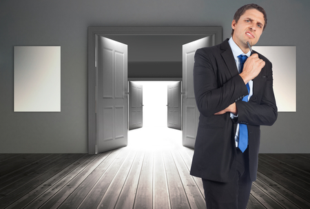 Thinking businessman holding pen against doors revealing bright lightの写真素材