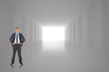 Serious businessman with hands on hips against digitally generated roomの写真素材