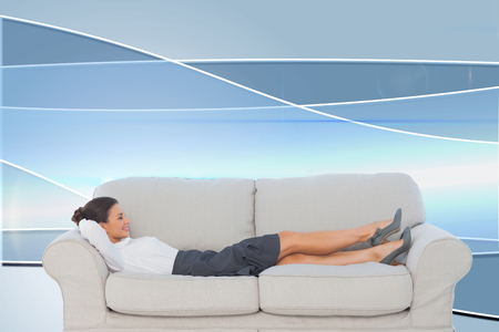 Composite image of smiling business woman lying down on the couch in the officeの写真素材