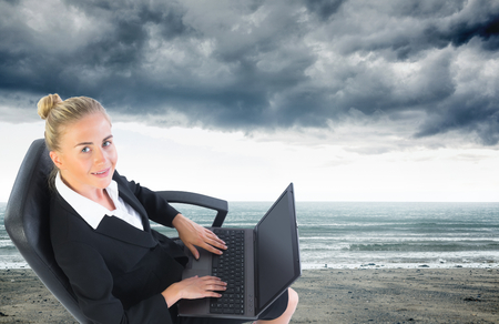 Composite image of blonde businesswoman sitting on swivel chair with laptopの写真素材