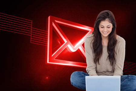 Composite image of beautiful smiling brunette sitting on floor using laptopの写真素材