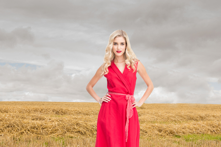 Composite image of elegant blonde standing hands on hips in red dressの写真素材