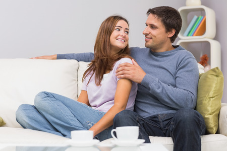 Relaxed loving young couple sitting on sofa and looking at each other at homeの写真素材