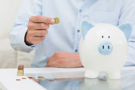 Close-up mid section of a man putting some coins into a piggy bank at homeの写真素材