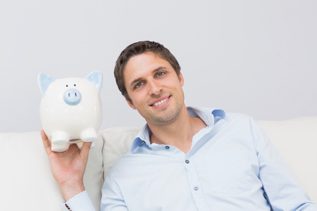 Handsome casual man with piggy bank in the living room at homeの写真素材