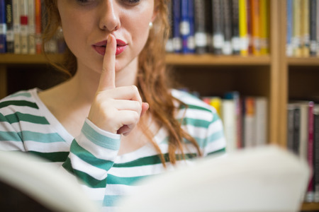 Redhead student asking for silence holding a book at the universityの写真素材