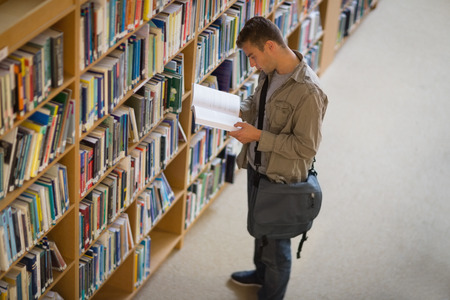 Student reading a book from shelf in library at the university