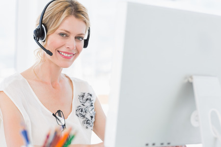 Portrait of a casual young woman with headset using computer in a bright office
