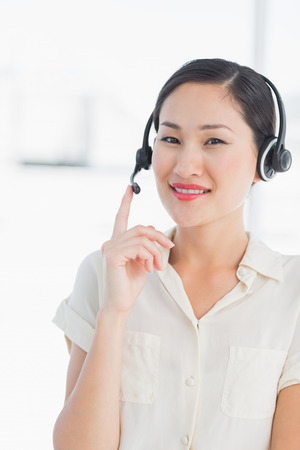 Portrait of a beautiful smiling female executive with headset in a bright officeの写真素材