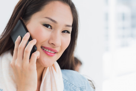 Close-up of a beautiful casual young woman using mobile phone in a bright officeの写真素材