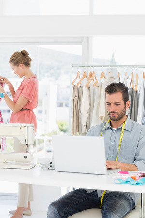 Young man using laptop with female fashion designer working in background at the studioの写真素材