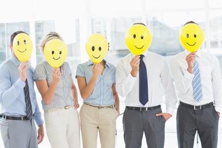 Group of business people holding happy smiles in front of their faces in a bright officeの写真素材
