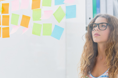 Concentrated female artist looking at colorful sticky notes at the office