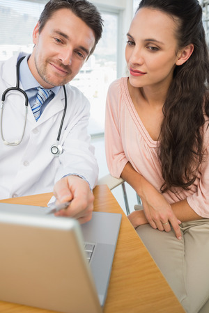 Male doctor showing something on laptop to patient at desk in medical officeの写真素材