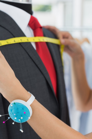 Extreme close-up of a female fashion designer measuring suit on dummy at officeの写真素材