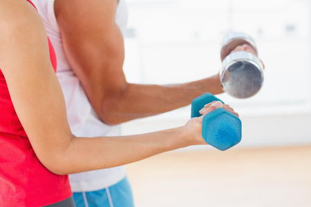 Closeup mid section of a sporty young couple with dumbbells in the gymの写真素材