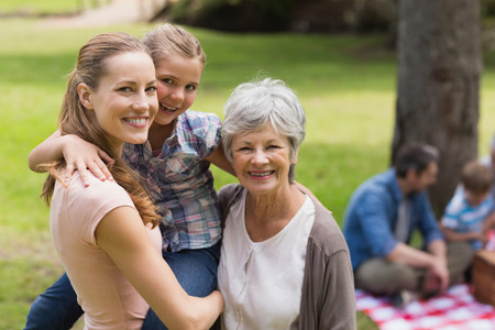Portrait of grandmother, mother and daughter with family in background at the park