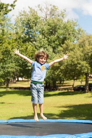 Full length of a happy boy jumping high on trampoline  in the parkの写真素材