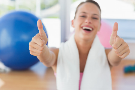 Portrait of a young woman with towel gesturing thumbs up in the gymの写真素材