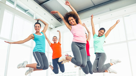 Full length portrait of fitness class and instructor jumping in fitness studioの写真素材