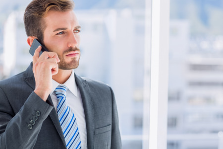 Handsome young businessman using mobile phone over blurred background in officeの写真素材