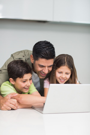 Father with young kids using laptop in the kitchen at homeの写真素材