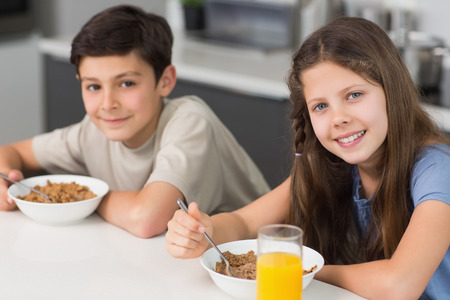 Portrait of two smiling young siblings enjoying breakfast in the kitchenの写真素材