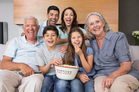 Portrait of happy extended family watching tv on sofa in the living room at home