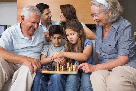 Happy extended family playing chess on sofa in the living room at home