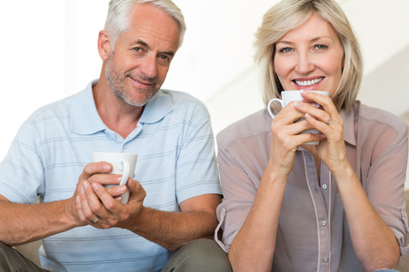 Portrait of a smiling mature couple with coffee cups sitting on sofa at homeの写真素材